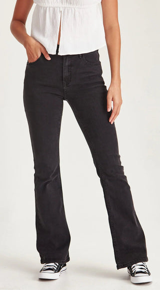 Woman wearing black flared denim jeans and a white sleeveless top.
