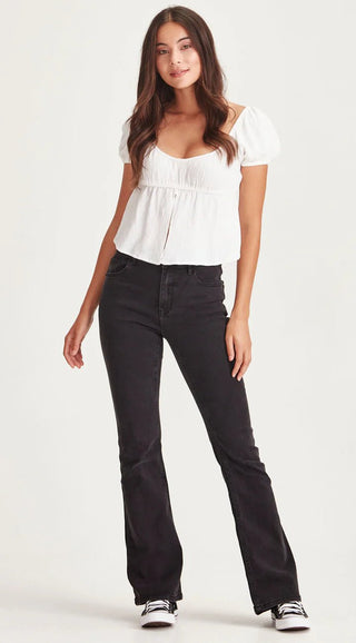 Woman wearing a white puff sleeve blouse and black flared denim jeans.