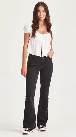 Woman wearing a white puff sleeve blouse and black flared denim pants.