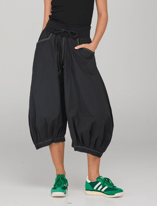 Woman wearing black wide-leg cropped harem pants and green sneakers.