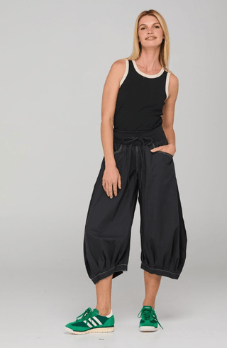 Woman wearing a black tank top with white trim and black cropped harem pants with green sneakers.