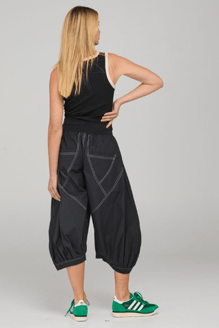 Woman wearing black tank top and loose black harem style cropped pants with green sneakers.