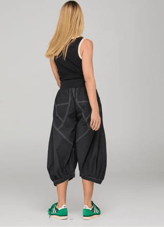 Woman wearing black oversized lounge pants with white stitching and a black sleeveless top.