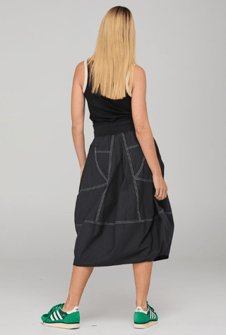 Back view of a woman wearing a black tank top, black contrast stitch midi skirt, and green sneakers