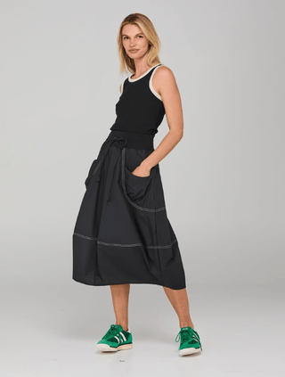 Woman wearing a black sleeveless top, black midi skirt with white stitching, and green sneakers.