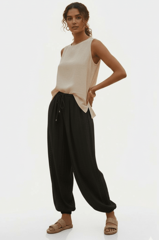 Woman wearing a beige sleeveless top and black drawstring harem pants with tan sandals.