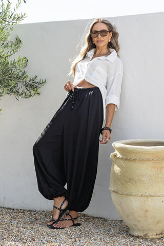 Woman wearing a white button-down shirt and black harem pants with strappy sandals.