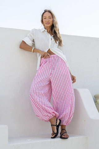 Woman wearing a white linen shirt and pink gingham checkered balloon pants.