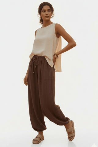 Woman wearing a cream sleeveless top and brown drawstring harem pants with sandals.