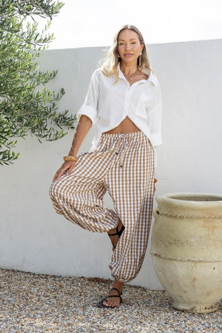 Woman wearing a white linen shirt and brown checkered wide-leg trousers.