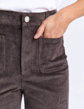 Close-up of a person wearing brown corduroy pants with a hand in the pocket.