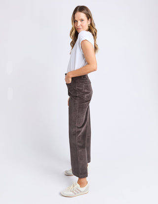 Woman wearing a white t-shirt and dark grey corduroy wide-leg pants with white sneakers.