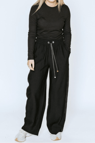 Woman wearing a black long sleeve top and wide leg black drawstring pants with white sneakers