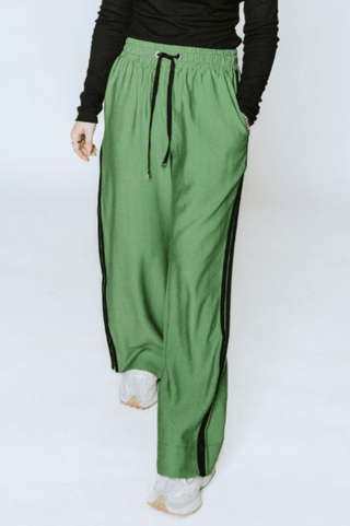 Woman wearing wide-leg green leisure pants with black side stripes and drawstring waist