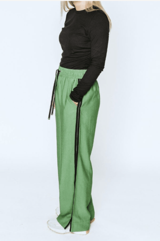 Woman wearing a black long sleeve top and green wide leg track pants with side stripes