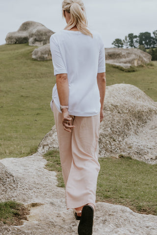 Woman from behind wearing a white t-shirt and beige wide-leg pants in a rocky landscape.