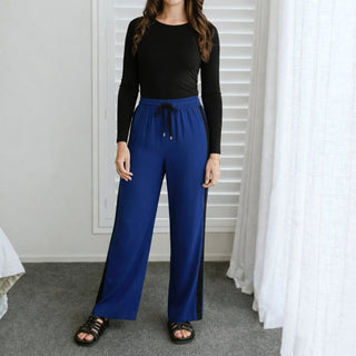 Woman wearing blue wide-leg lounge pants with black side stripes and a black long-sleeve top.
