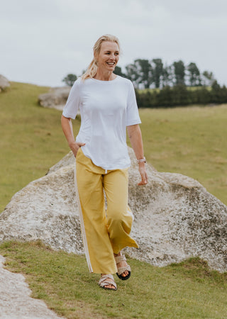 Woman in a white t-shirt and yellow wide-leg trousers walking in a grassy field.