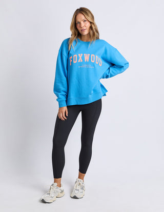 Woman wearing a blue Foxwood sweatshirt and black leggings with white sneakers.