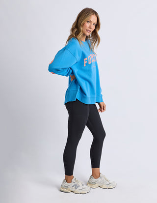 Woman wearing a blue graphic sweatshirt and black leggings with white sneakers.