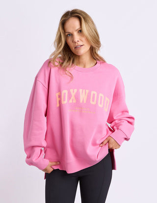 Woman wearing a pink Foxwood oversized sweatshirt and black trousers.