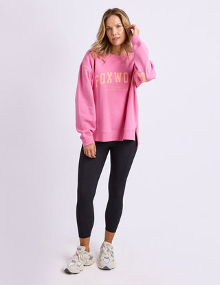 Woman wearing a pink Foxwood sweatshirt and black leggings with white sneakers.