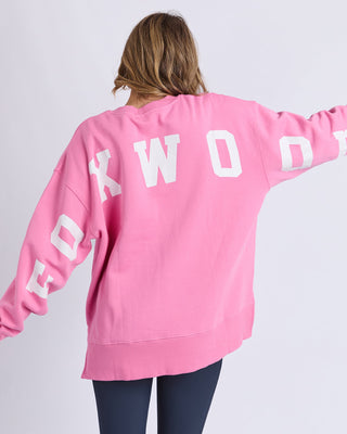Back view of a woman wearing a pink Foxwood oversized sweatshirt with white lettering.