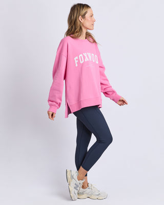 Woman wearing a pink Foxwood sweatshirt and navy leggings with white sneakers.