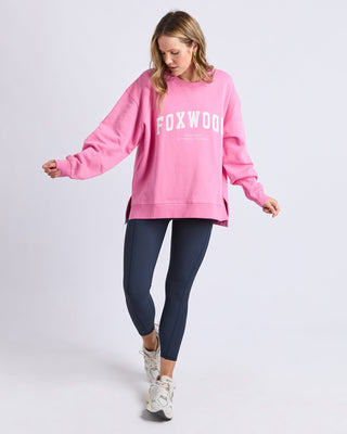 Woman wearing a pink Foxwood sweatshirt, navy leggings, and white sneakers.