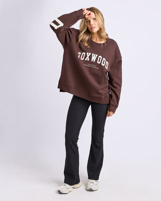 Woman wearing a brown Foxwood sweatshirt and black flared leisure pants.