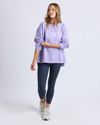 Woman wearing a purple Foxwood sweatshirt, navy leggings, and white sneakers.