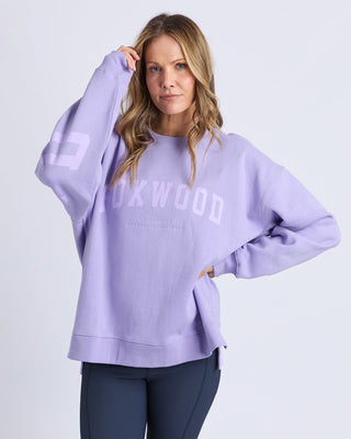 Woman wearing a purple Foxwood oversized sweatshirt and dark blue leggings.
