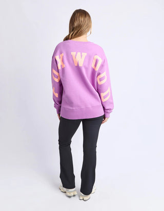 Woman wearing a purple Foxwood sweatshirt and black flare pants from behind.