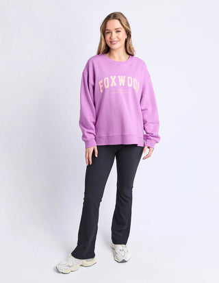 Woman wearing a purple Foxwood sweatshirt, black flare pants, and white sneakers.