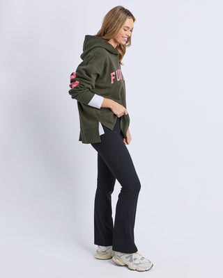 Woman wearing an olive green Foxwood hoodie and black flared yoga pants with sneakers.