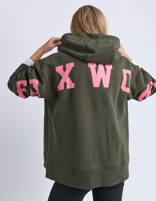 Woman wearing an oversized olive green Foxwood sweatshirt with pink graphic lettering on the back.