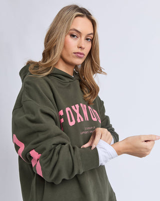 Woman wearing an olive green Foxwood graphic hoodie with pink lettering.