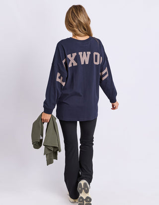 Woman wearing a navy blue Foxwood oversized long sleeve sweatshirt and black pants.