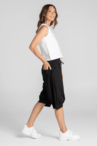 Woman wearing a white sleeveless top and black cropped harem pants with white sneakers.