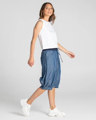 Woman wearing a white sleeveless top and blue denim cropped harem pants with white sneakers.