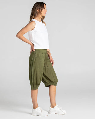 Woman wearing a white sleeveless top, olive green cropped joggers, and white sneakers.