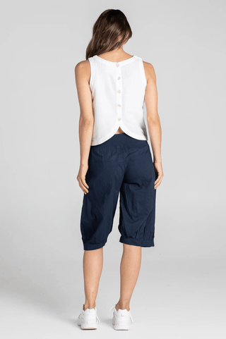 Back view of a woman wearing a white button-down sleeveless top and navy cropped pants.