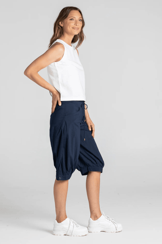 Woman wearing a white sleeveless top and navy blue cropped joggers with white sneakers.