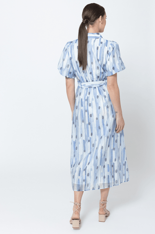 Back view of a woman wearing a blue and white abstract print midi dress with a waist tie.