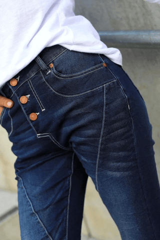 Woman wearing dark blue denim jeans with decorative button detailing on the waist.