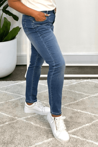 Woman wearing slim-fit blue denim jeans and white sneakers standing on a grey rug.