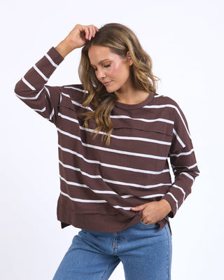 Woman wearing a brown and white striped long sleeve sweatshirt and blue jeans.