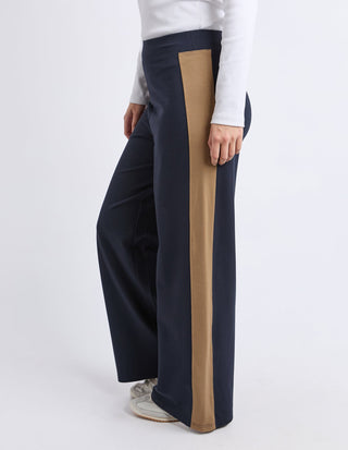Woman wearing navy blue wide-leg palazzo pants with a tan side stripe.