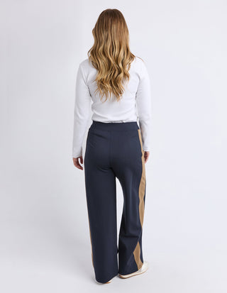 Woman wearing a white long sleeve top and navy blue wide leg pants with tan side stripes.