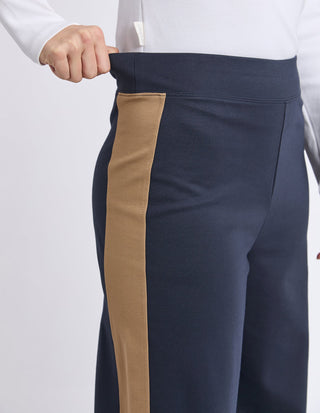 Woman wearing navy blue leisure wear pants with a tan side stripe detail.